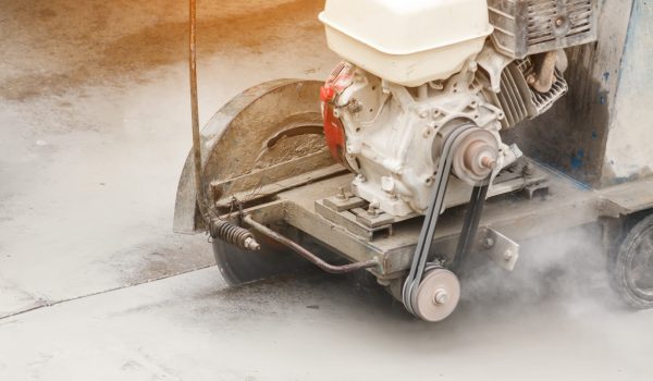 Worker using diamond saw blade machine cutting concrete road at construction site